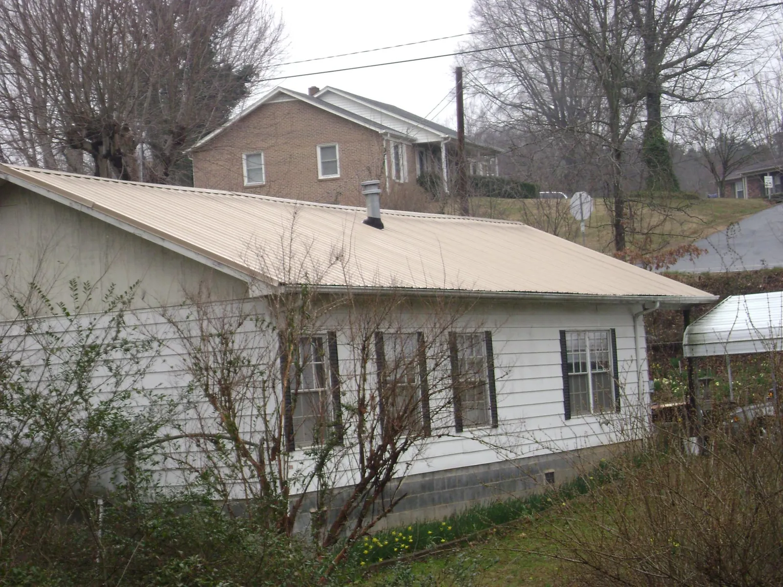Tan metal roof on a white sided house set into a hillside in Marysville